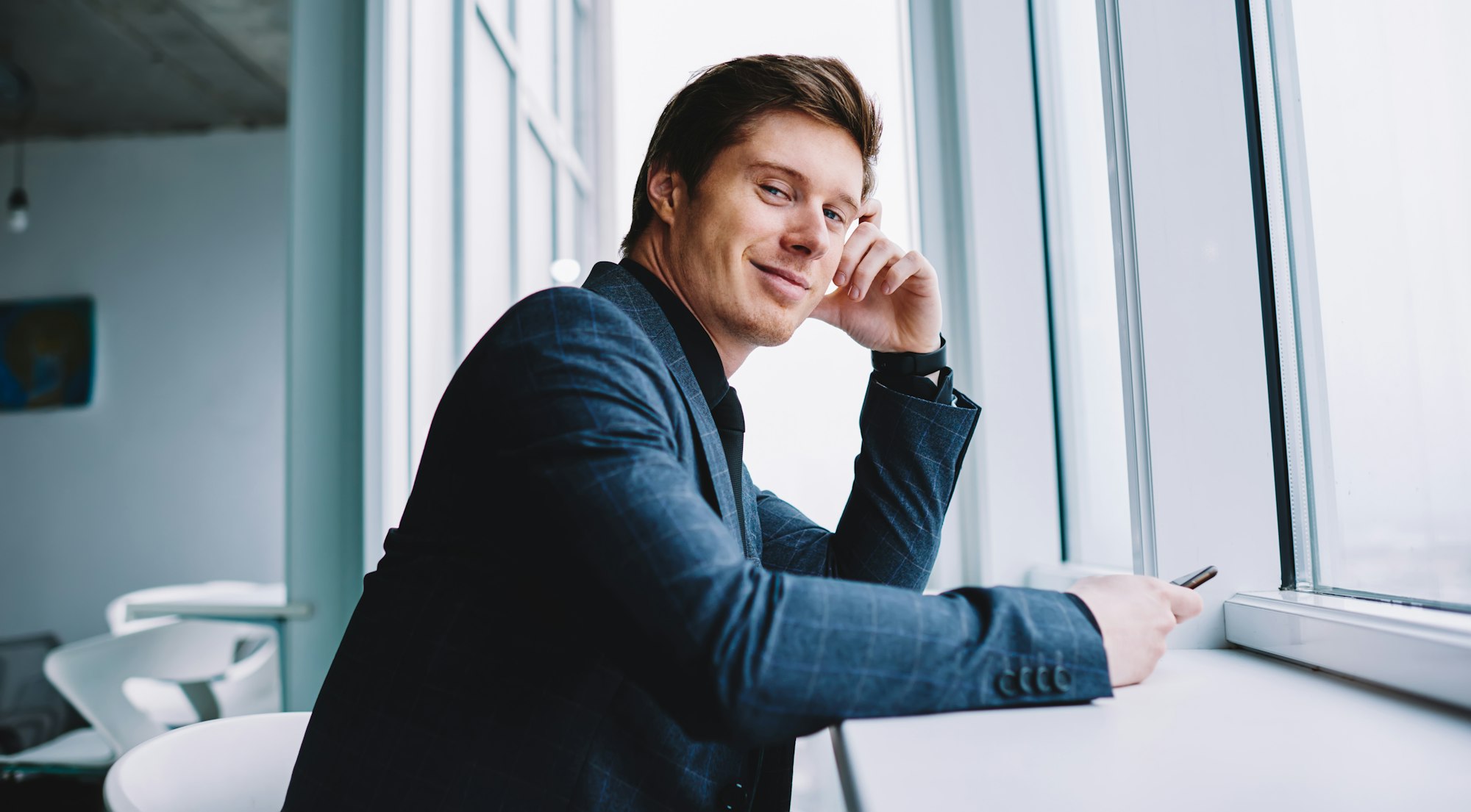 handsome confident male entrepreneur holding cellphone technology in hand and posing indoors